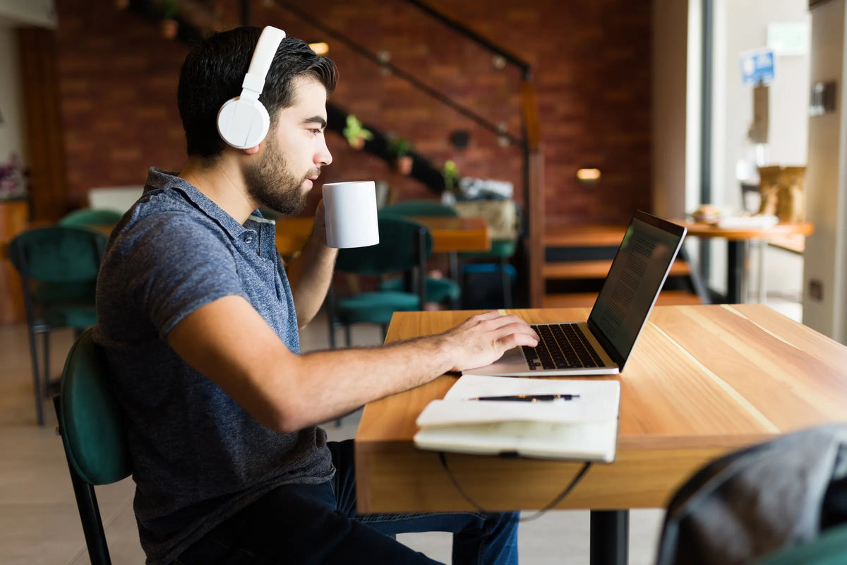 Hombre con audífonos estudiando en su laptop en una cafetería
